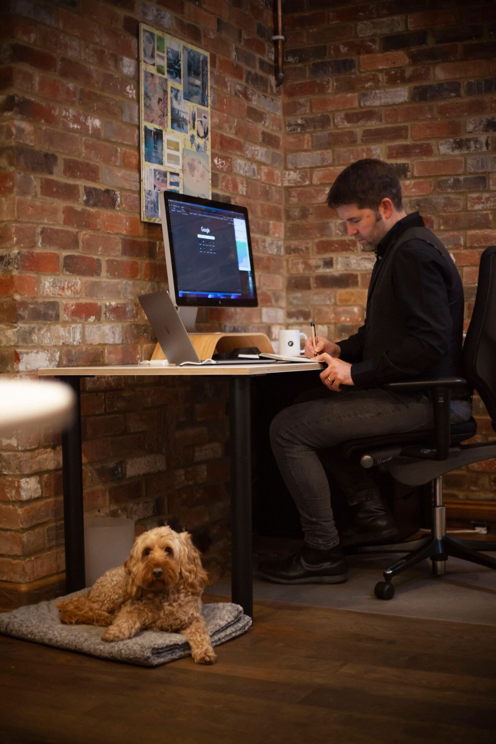 man sat at desk inside red brick building with dog at his feet